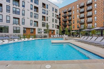 A large outdoor swimming pool surrounded by lounge chairs and buildings.